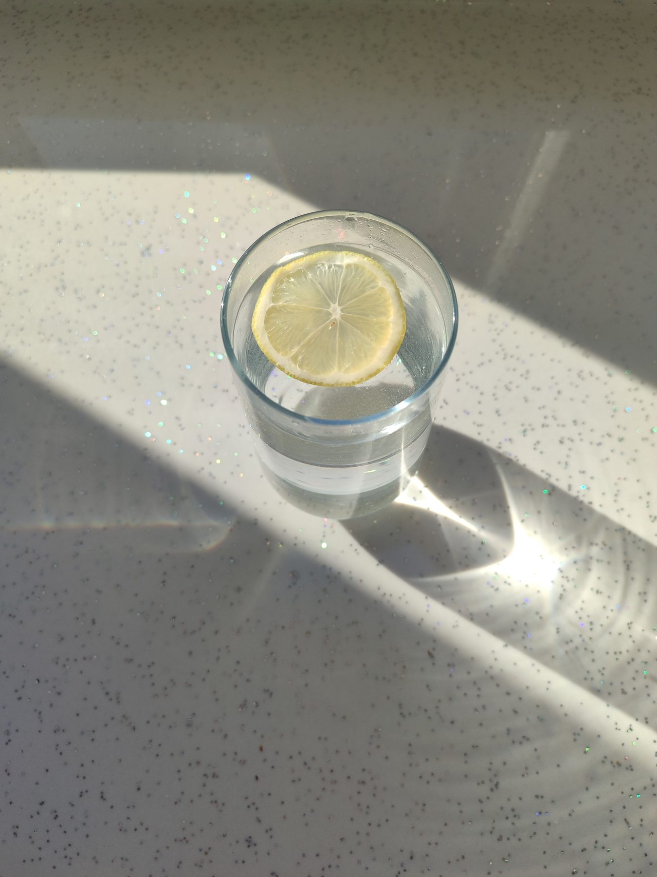 Glas Wasser mit Zitronenscheibe im Sonnenlicht