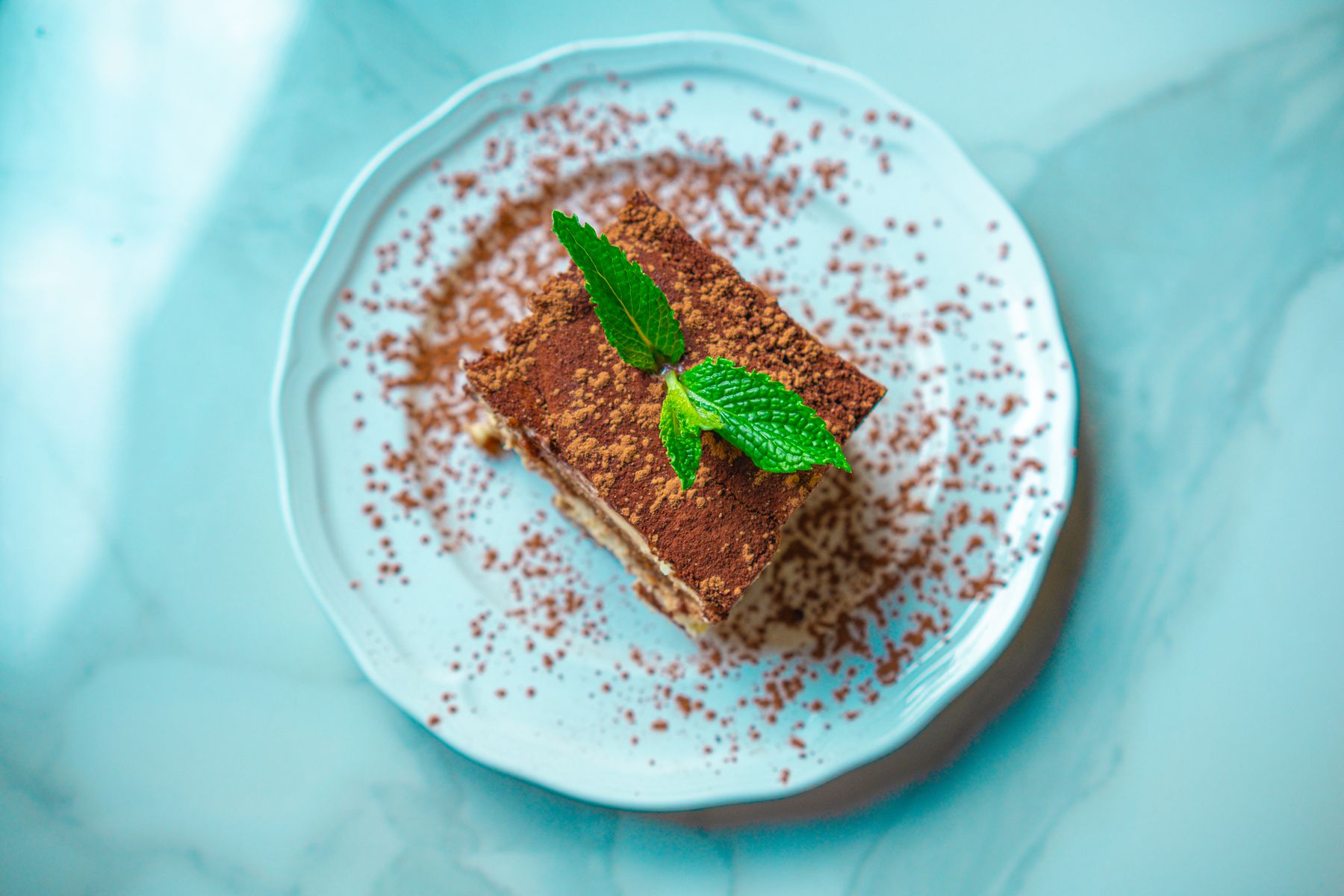 Tiramisu-Stück mit Kakaopulver und Minze auf einem Teller, Aufsicht