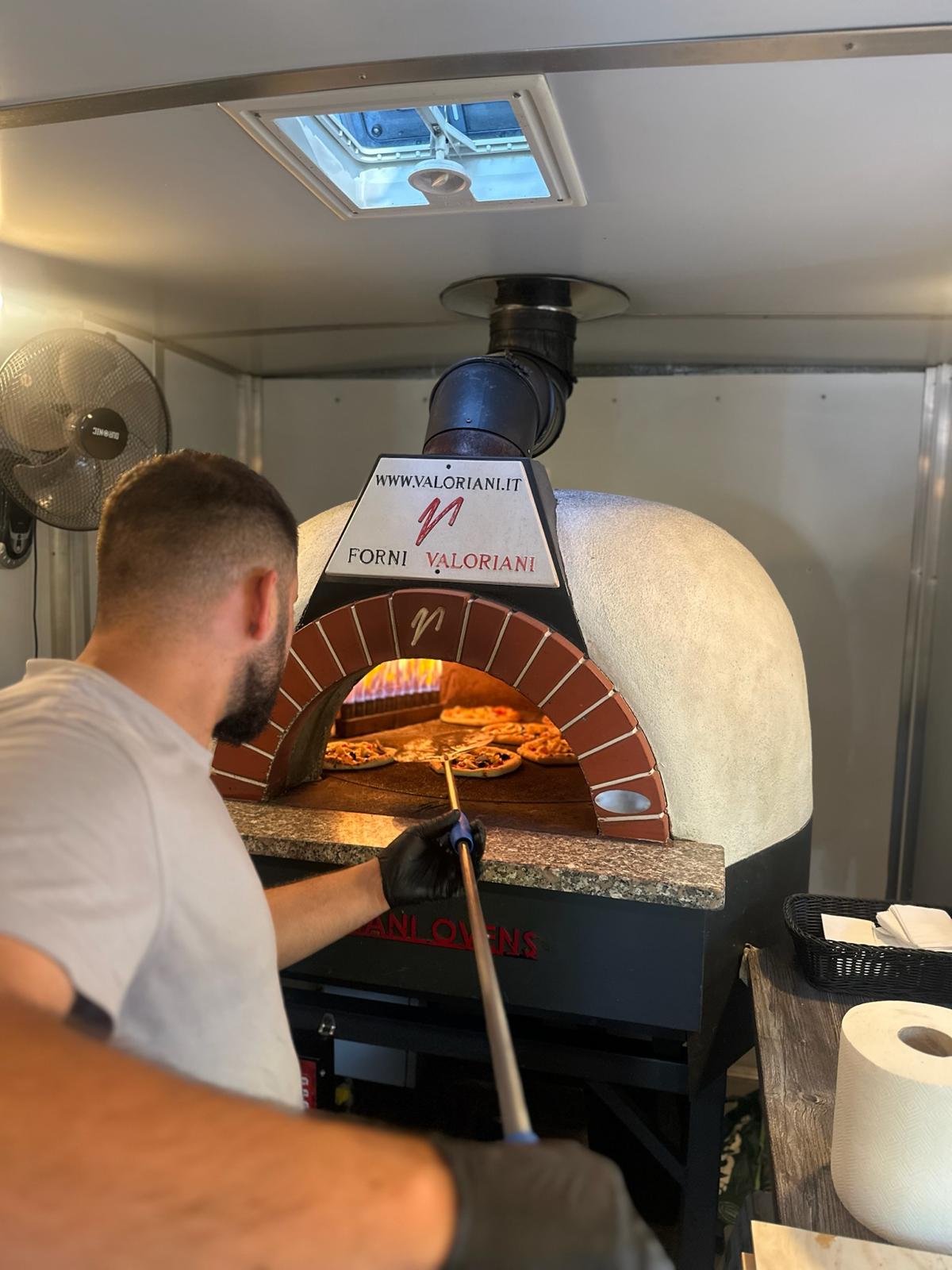 Pizzabäcker schiebt Pizzen mit dem Holzschieber in den Steinofen